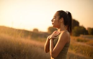 a woman breathing deep with her hands on her chest at sunset