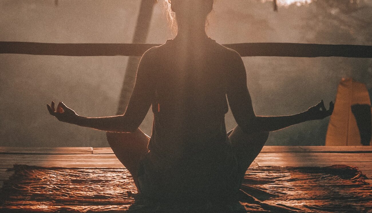 Woman practicing yoga outdoors at sunrise with a serene natural landscape
