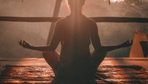 Woman practicing yoga outdoors at sunrise with a serene natural landscape