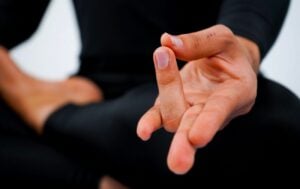 Hands forming Surya Mudra, the yogic fire gesture, resting on the knees during seated meditation